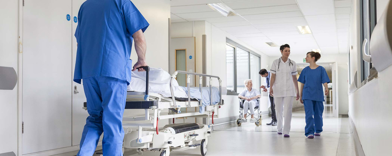 Male nurse pushing stretcher gurney bed in hospital corridor with doctors & senior female patient