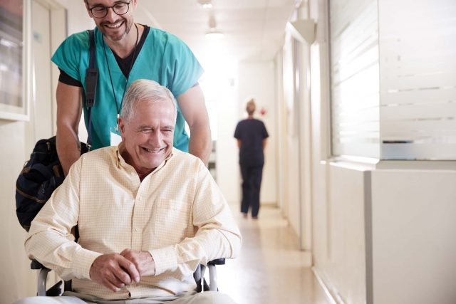 male nurse pushes older gentleman down hallway in wheelchair