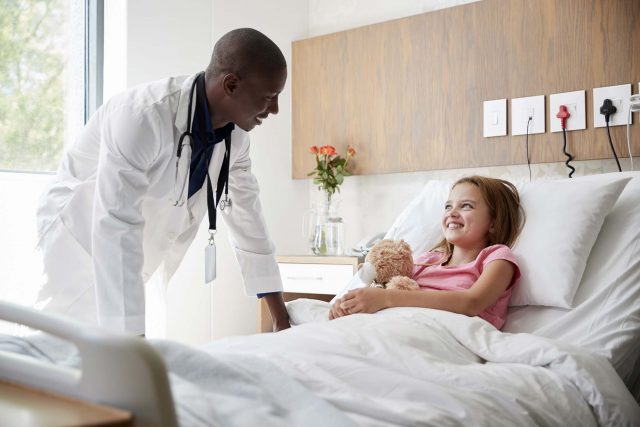 male doctor checks in on pediatric patient holding a stuffed bear