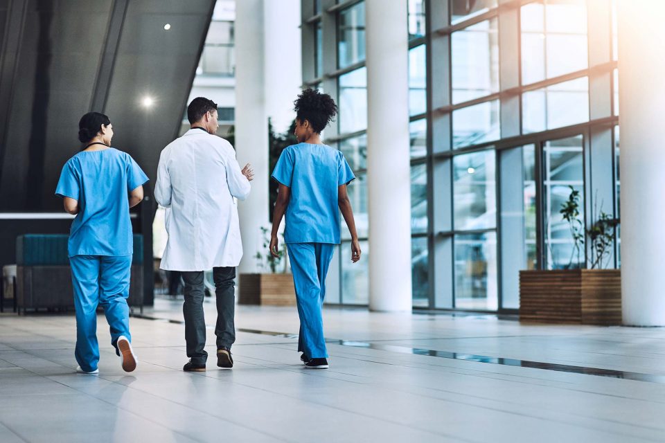 medical practitioners have a conversation walking down hallway of hospital