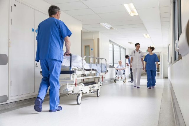 man pushes stretcher down hallway of hospital